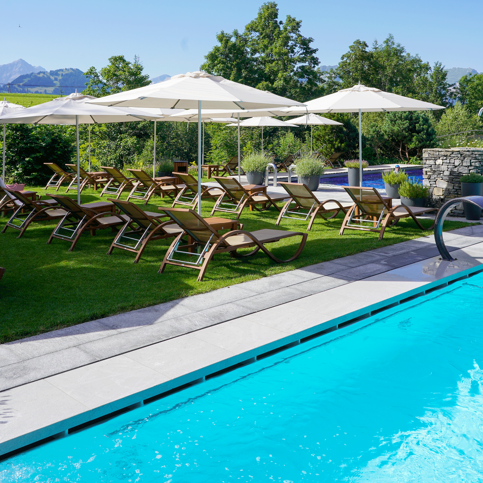 Sunbathing lawn at the Hotel Ermitage Sunbathing lawn with deckchairs and parasols next to the light blue pool