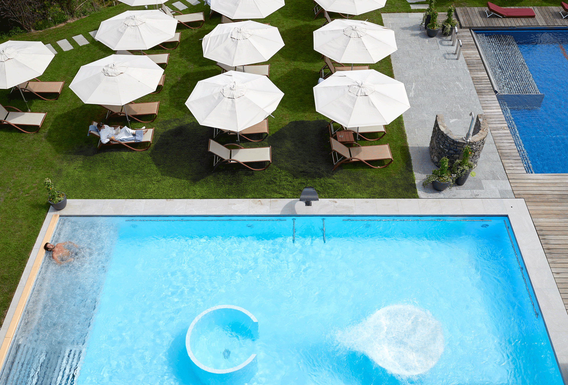 A light blue and dark blue pool and a lawn with sunbeds and parasols