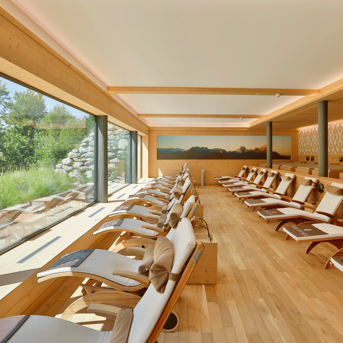Relaxation room in the sauna at the Hotel Ermitage Two rows of loungers in front of a large panoramic window with a view of the greenery