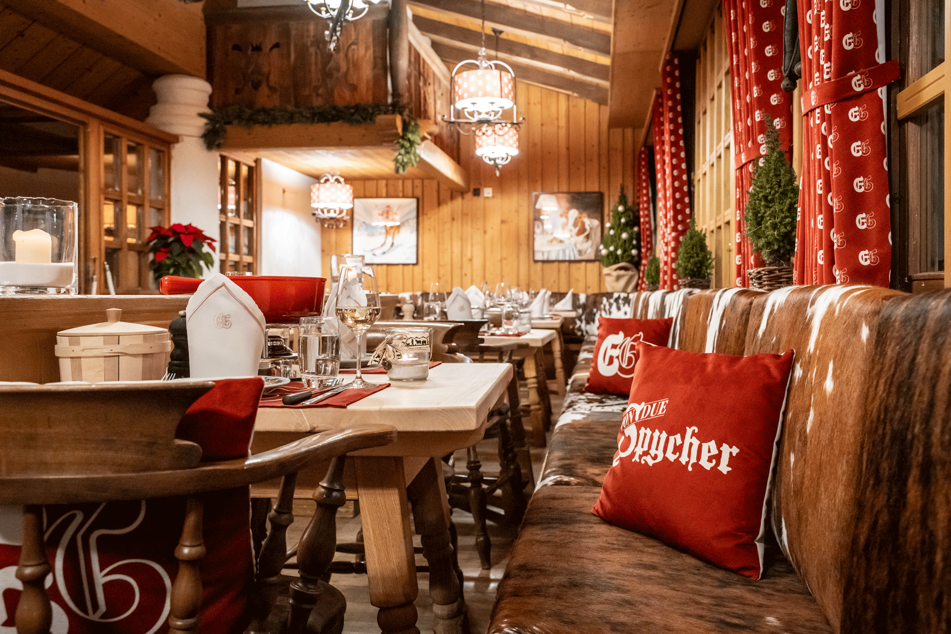 Restaurant à l'aménagement rustique avec beaucoup de bois, de peaux de vache, de coussins et de rideaux rouges, tables nappées