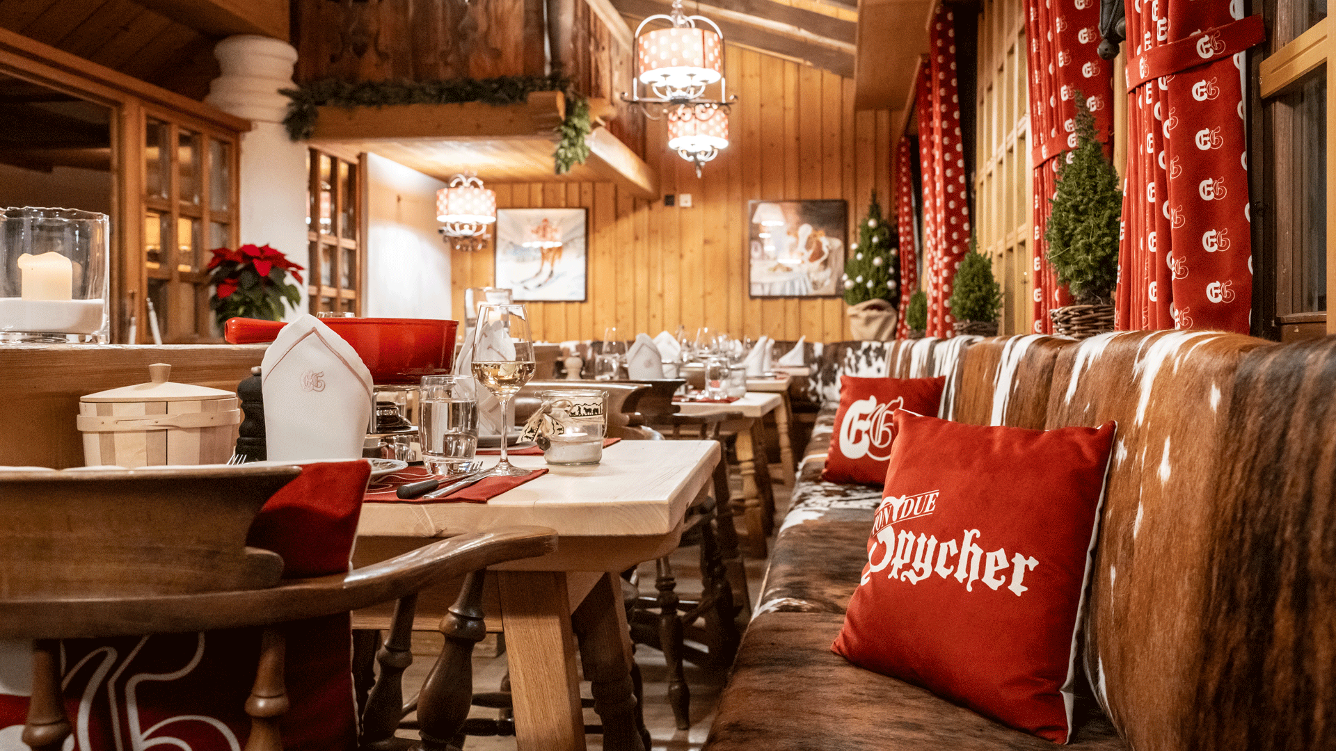 Fondue Spycher at the Hotel Ermitage Rustic restaurant with lots of wood, cowhides, red cushions and curtains, laid tables