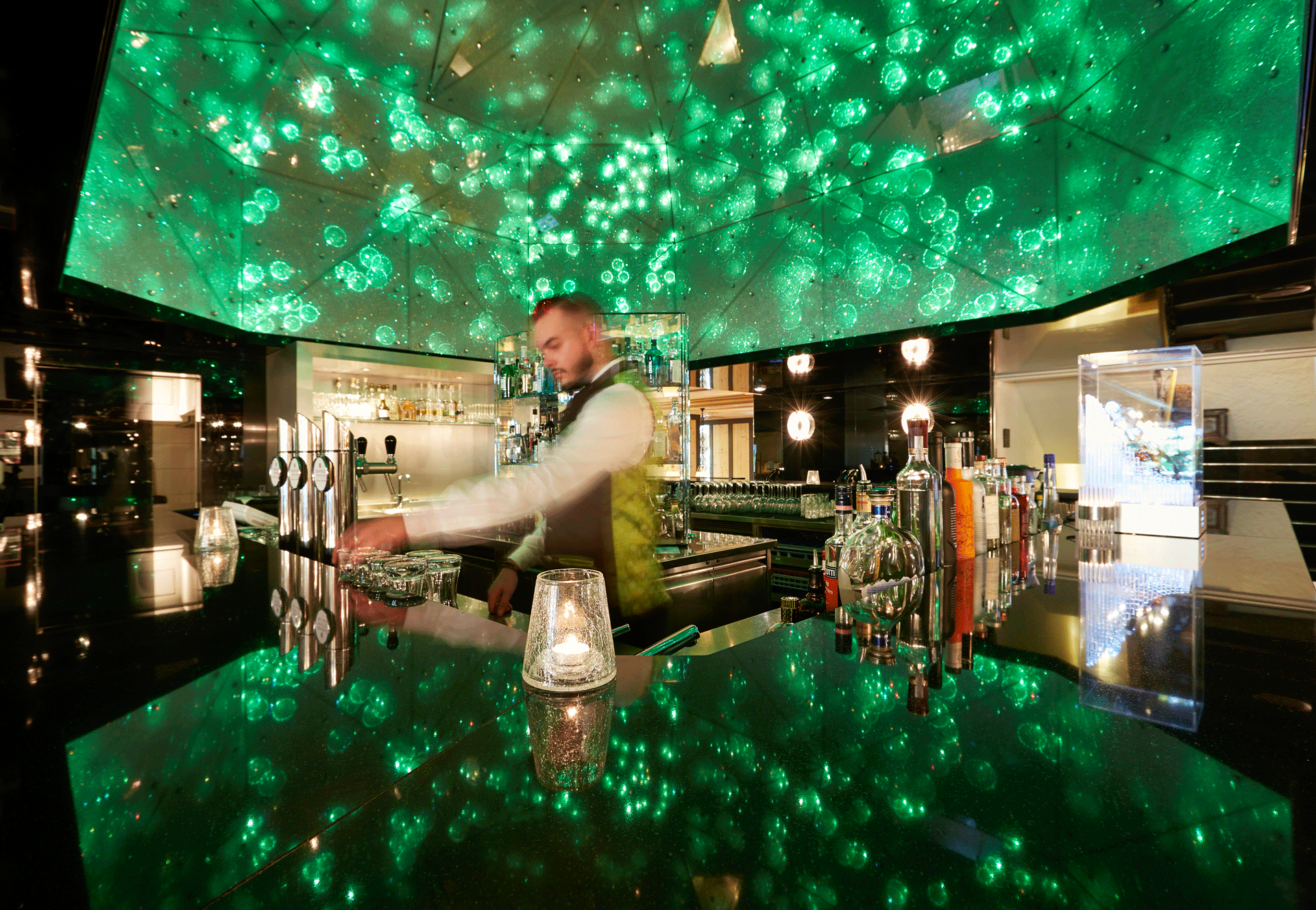 Kellner hinter einer grün beleuchteten funkelnden Bar