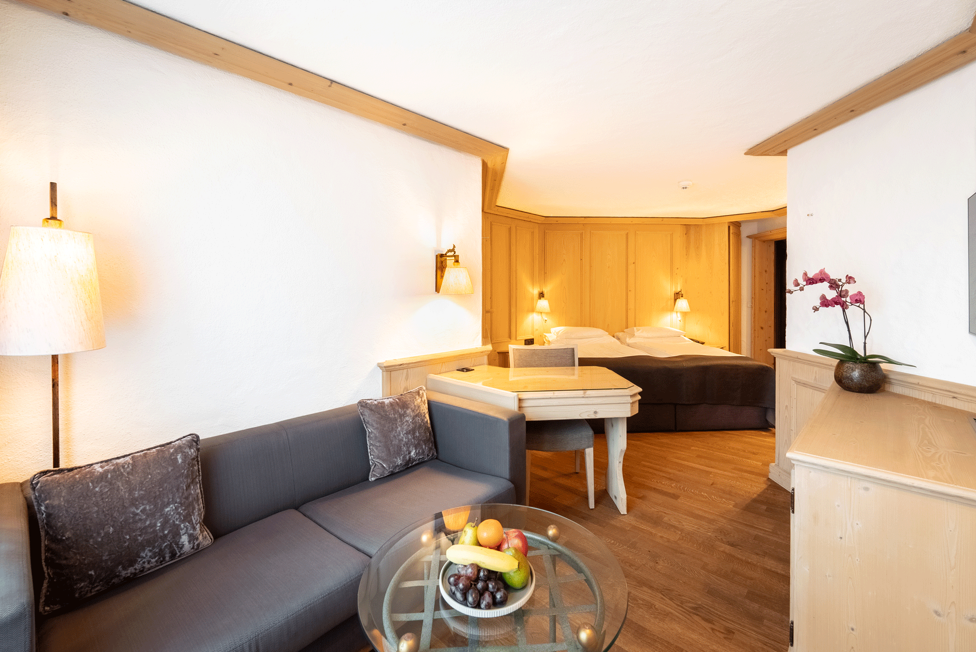 Wohnecke mit Sofa und Glastisch, im Hintergrund der Schlafbereich mit Doppelbett