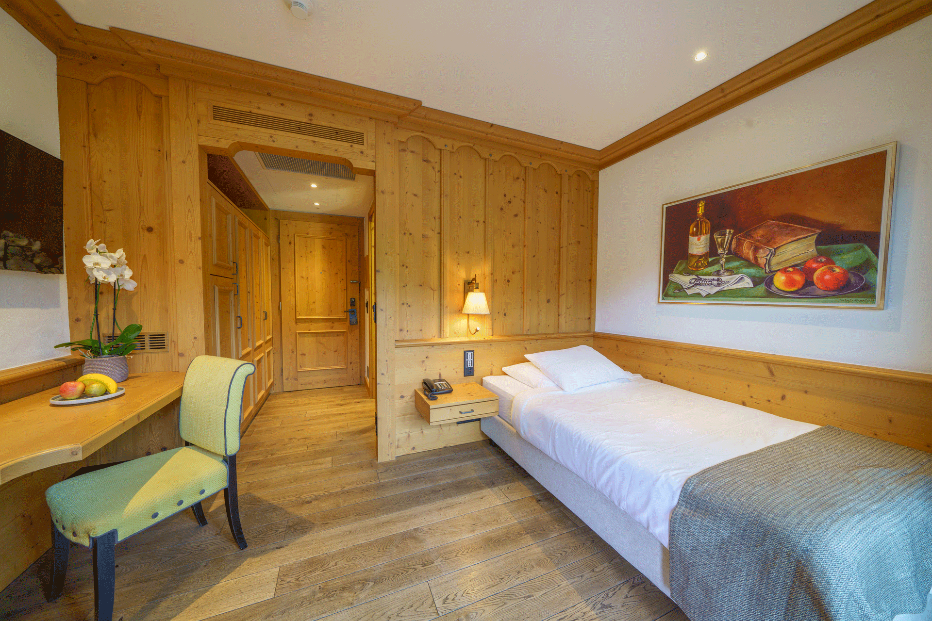 Zimmer mit Einzelbett, Holzwand, Holzboden, Tisch und Polstersessel