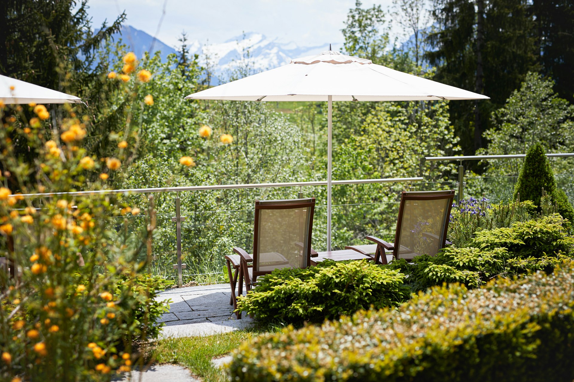 Deux chaises longues et un parasol entre des parterres de fleurs et des haies