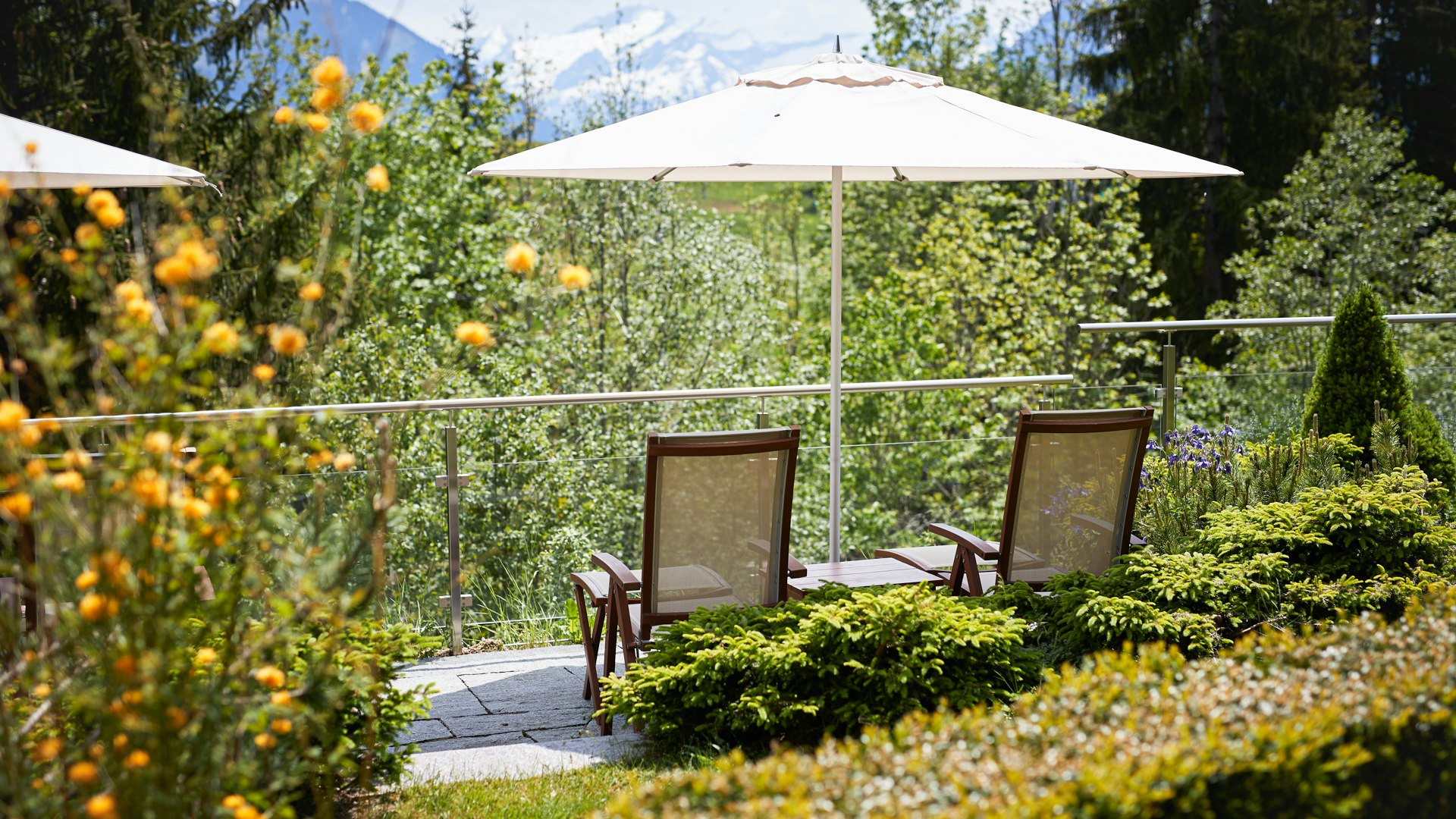 Park at Hotel Ermitage Two sunbeds and parasol between flowerbeds and hedges