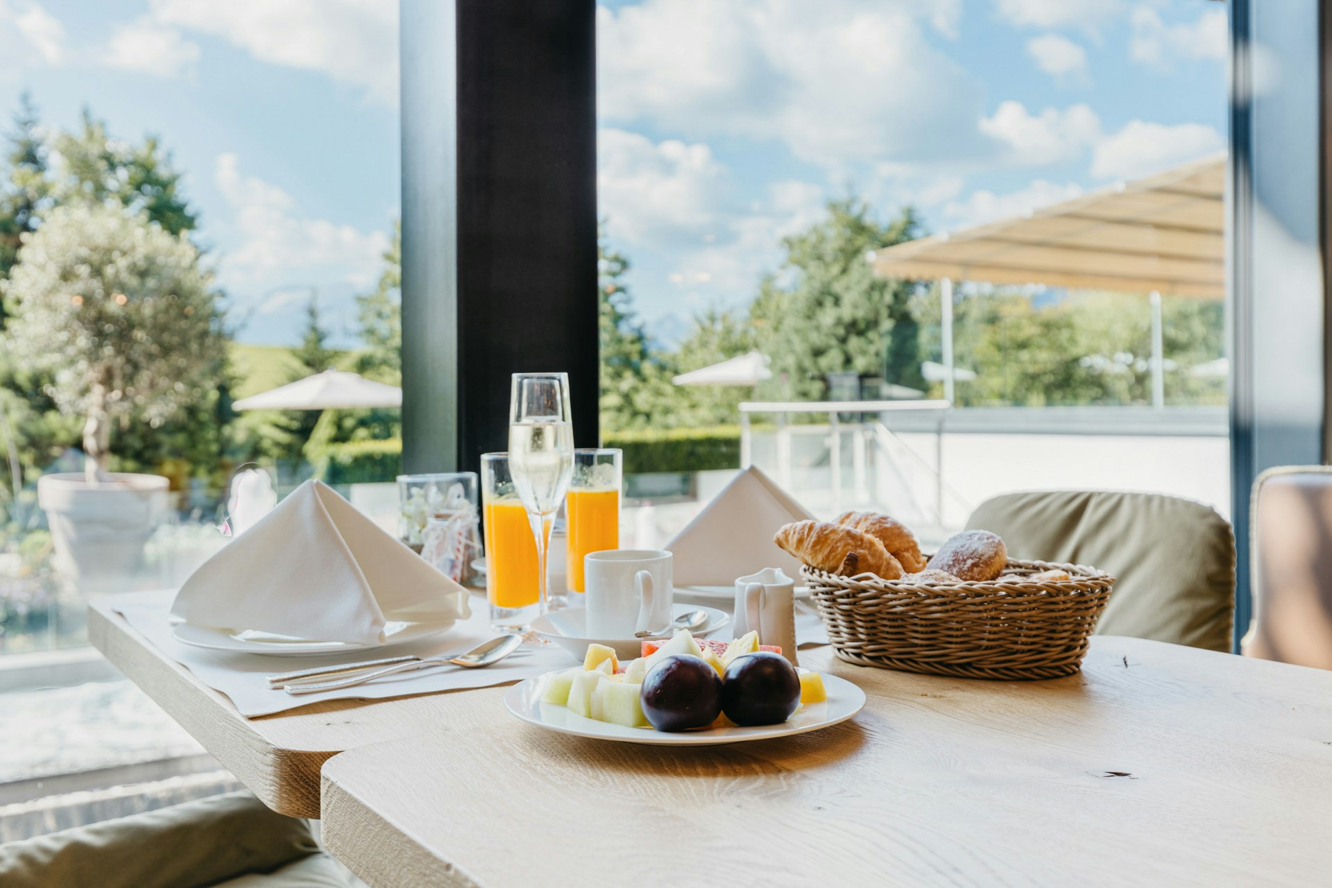Breakfast with sparkling wine and orange juice on a table, behind a large window with a view of the garden