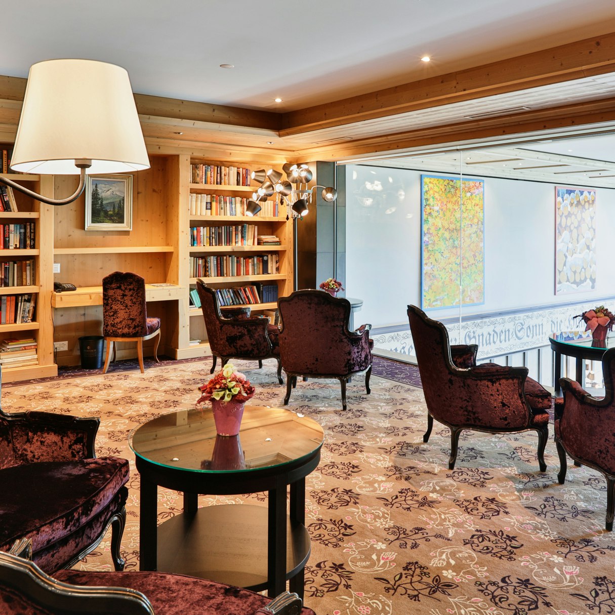 Läsi-Stube seminar room and library in the Hotel Ermitage Cosily furnished room with a wall of books and a large window overlooking the hotel lobby