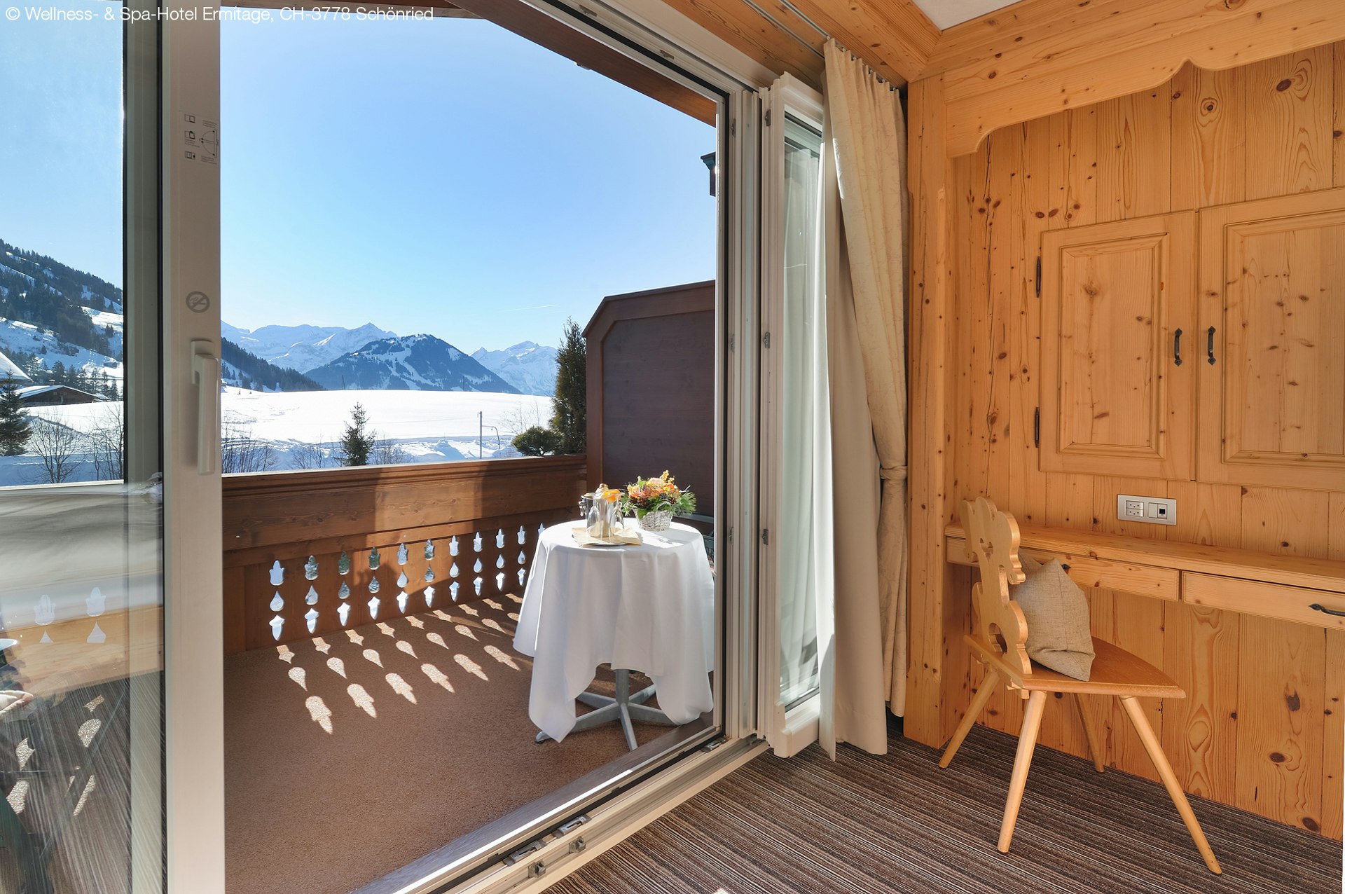 Holzgetäfertes Zimmer mit Blick auf einen sonnigen Balkon und Schnee