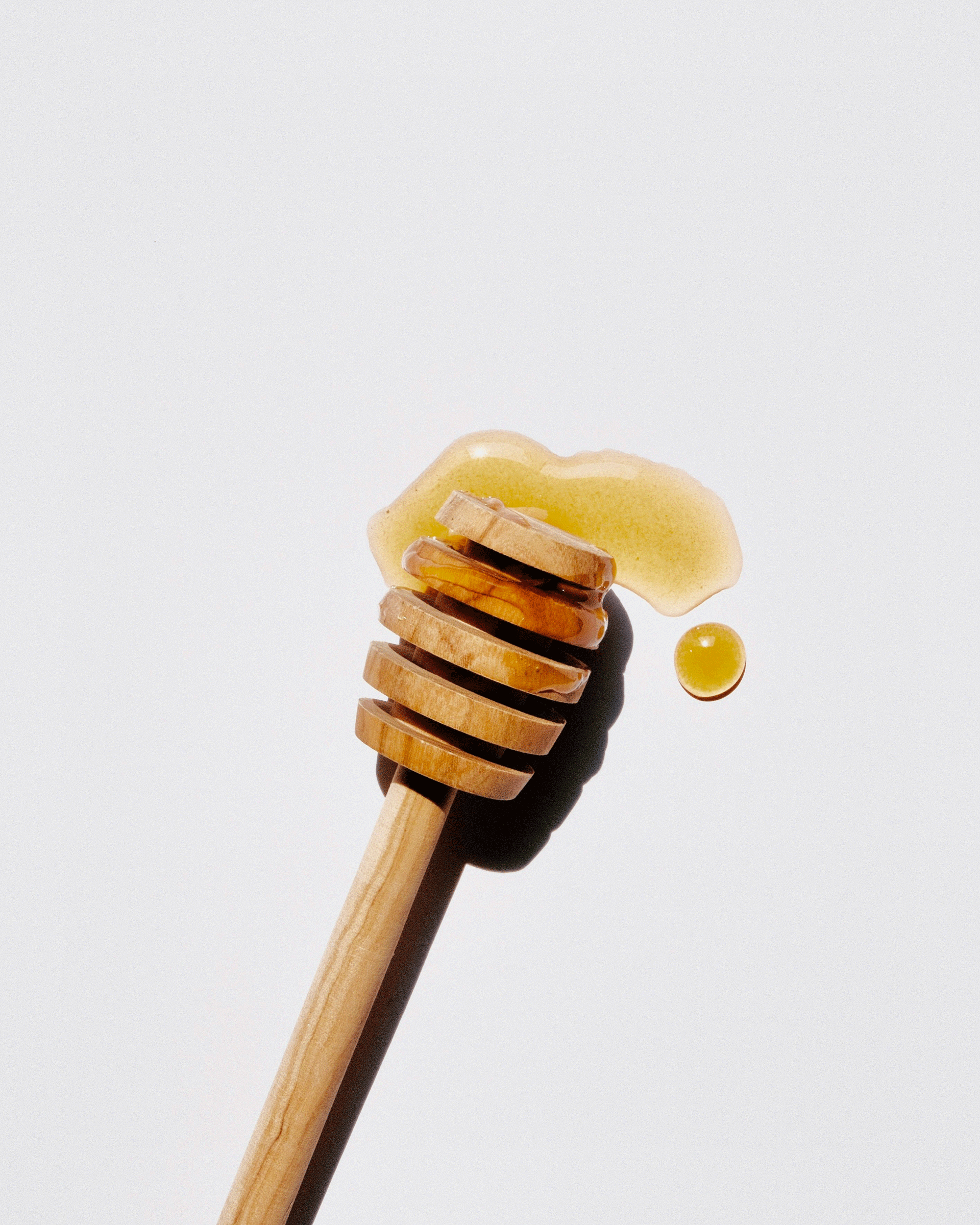 Miel sur cuillère à miel en bois, fond neutre, lumière contrastée