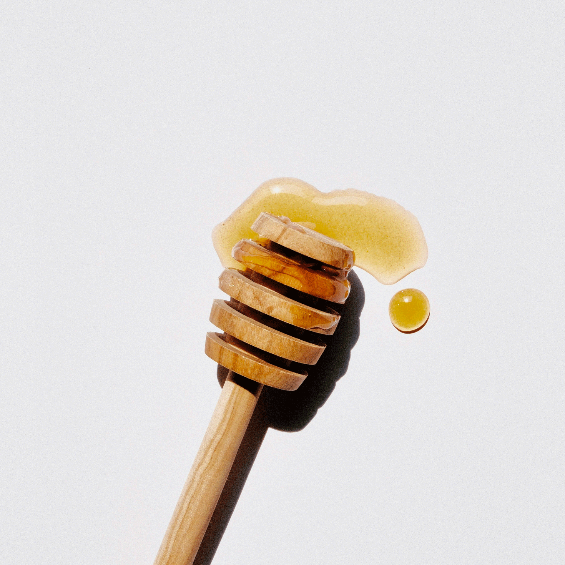 Ermitage kitchen philosophy Honey on a wooden honey spoon, neutral background, high-contrast light