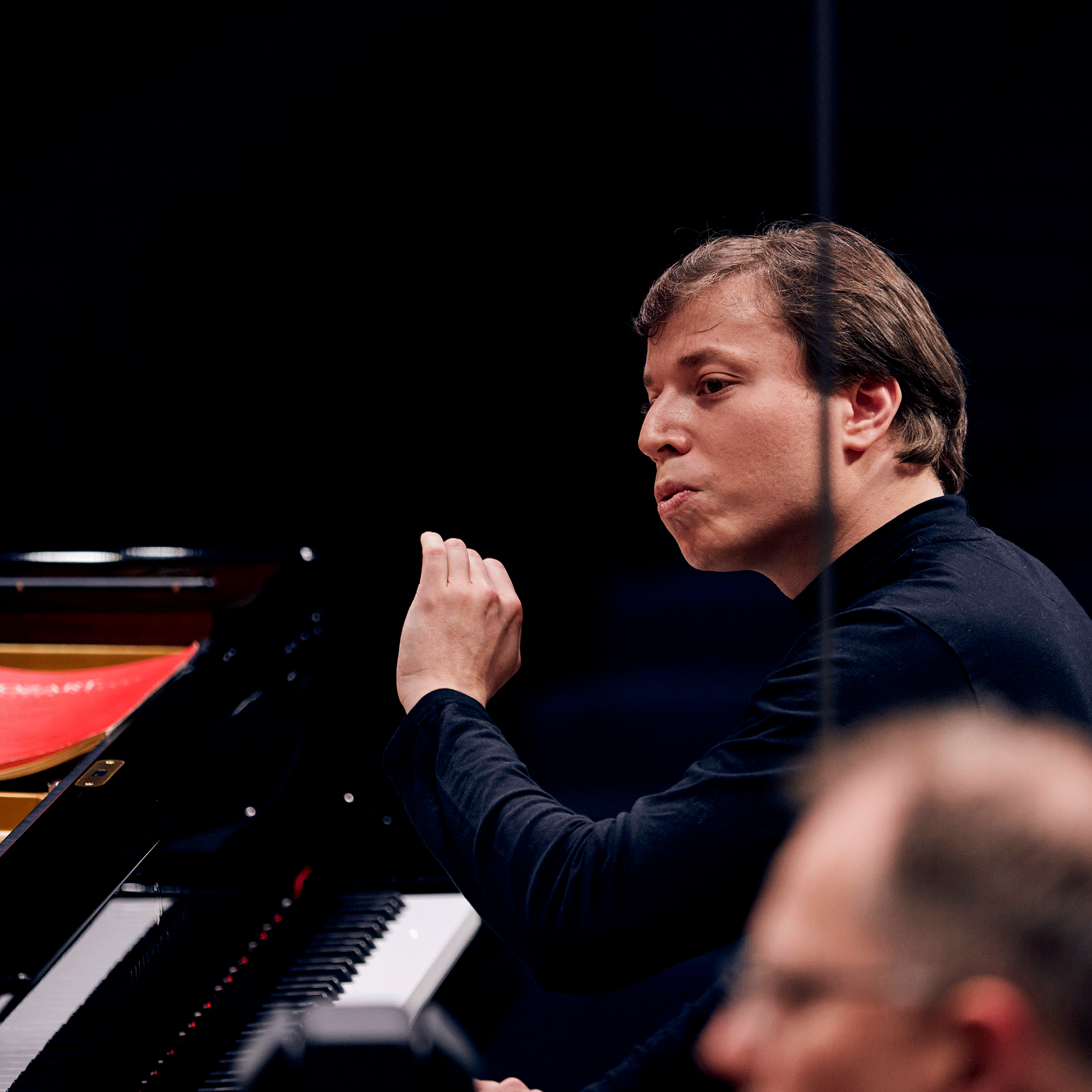 Gstaad Menuhin Festival Chef d'orchestre devant un piano, au premier plan dans le flou un violoniste
