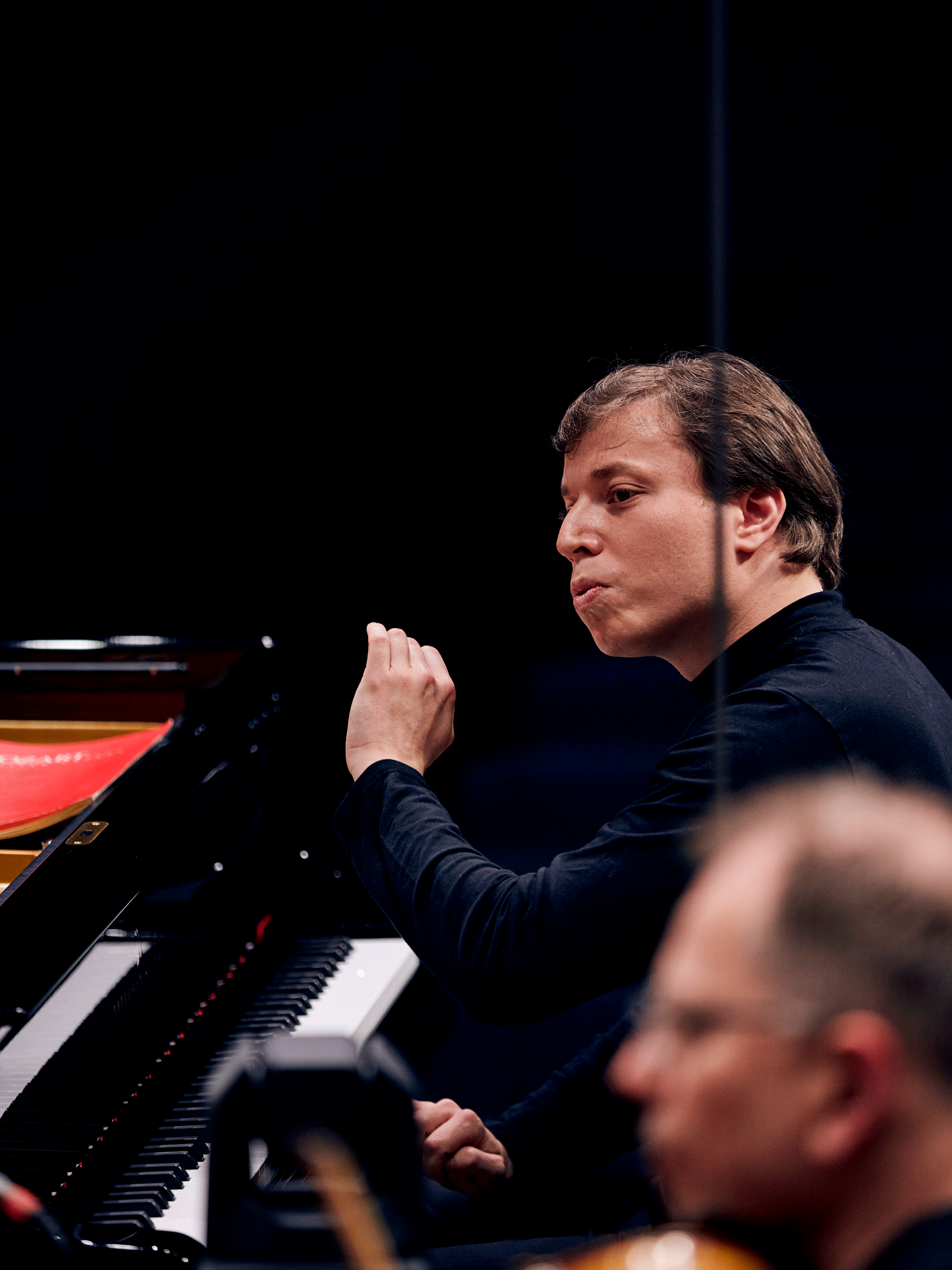 Gstaad Menuhin Festival Conductor in front of piano, in the foreground in the blur a violinist