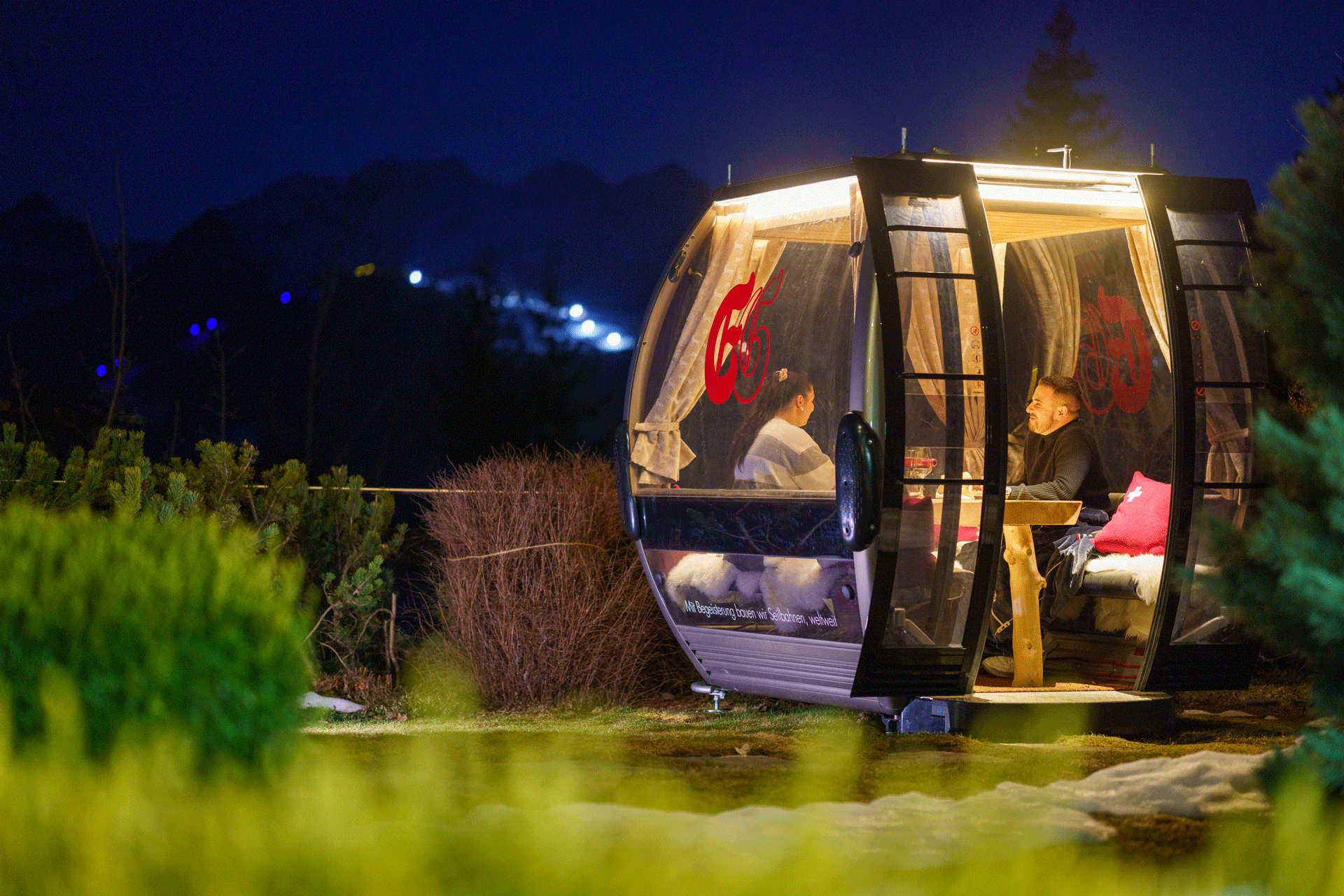 Gondel steht auf der Wiese in der Nacht, darin zwei Menschen beim Essen