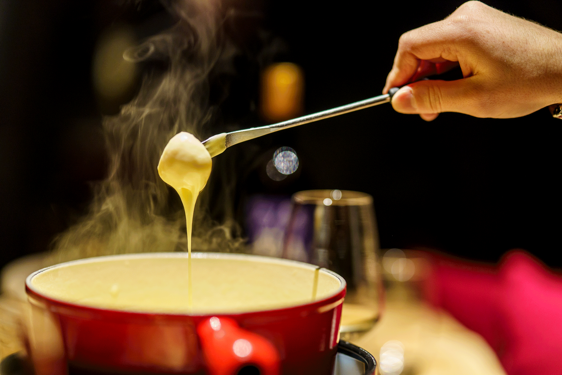 Jemand zieht eine Gabel aus dem Fondue-Caquelon