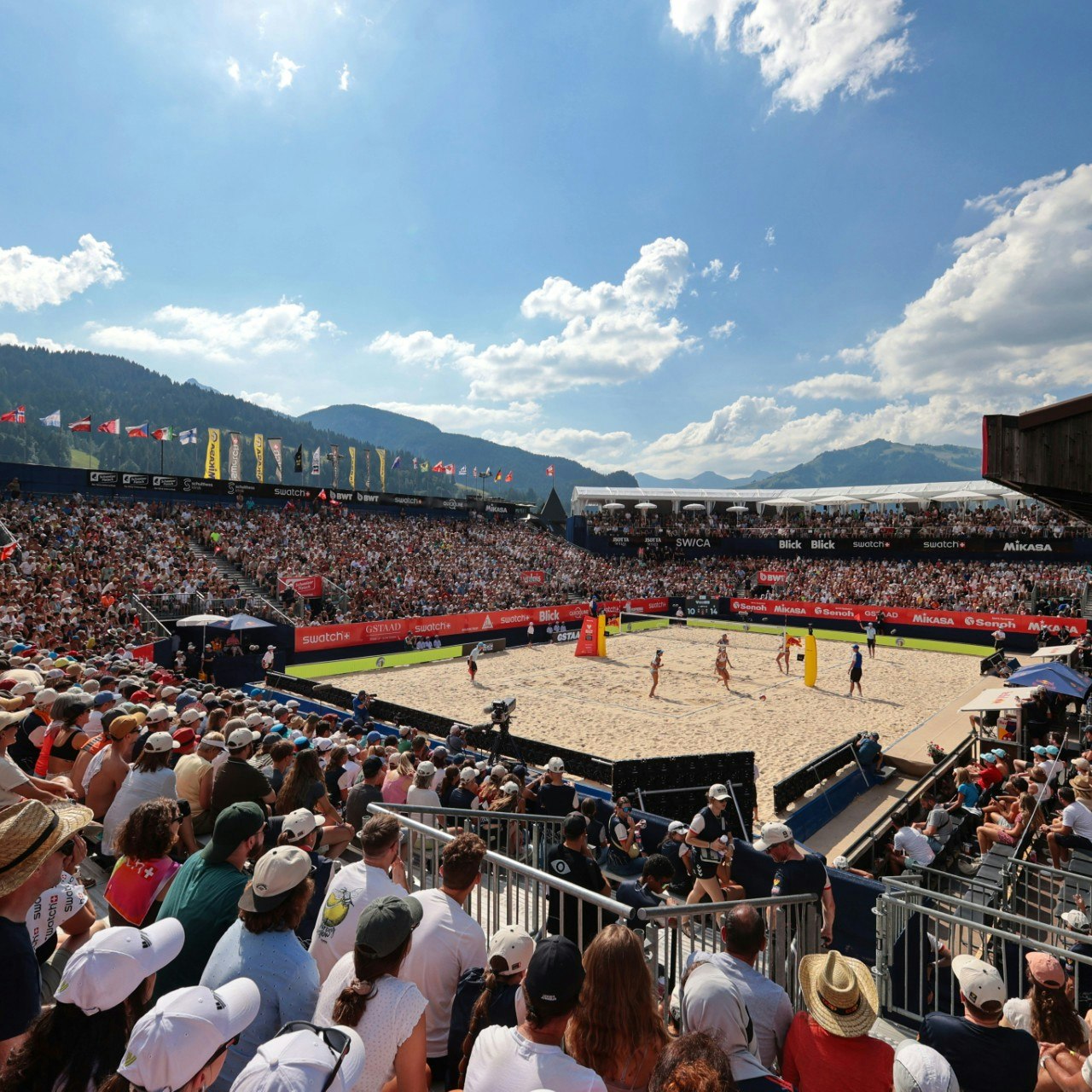 Volley Gstaad A packed stadium with a volleyball court in the middle, excited spectators watching the volleyball match.
