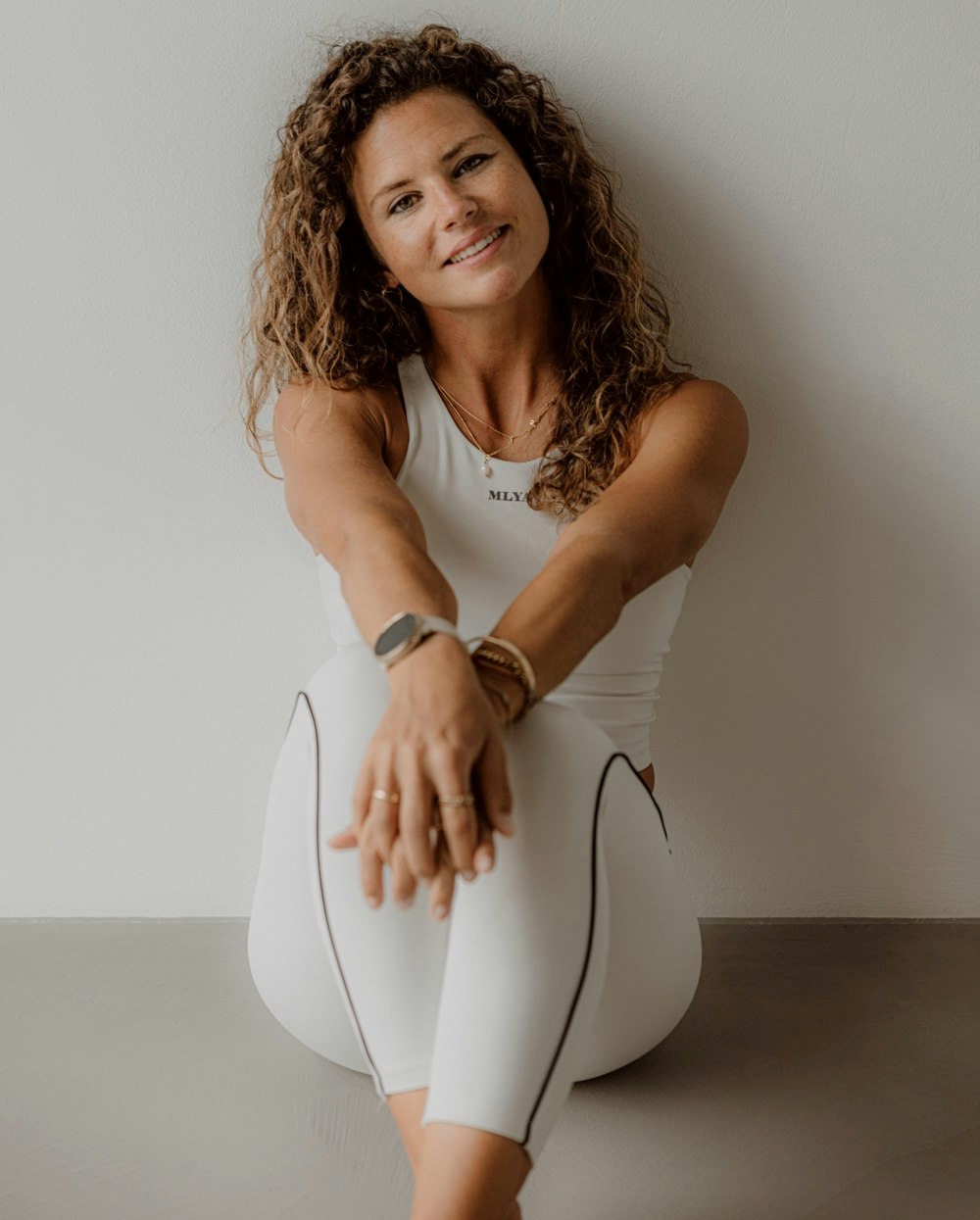 Laura Müdespacher A woman sitting on the floor, her arms folded, smiling at the camera. She is wearing white.