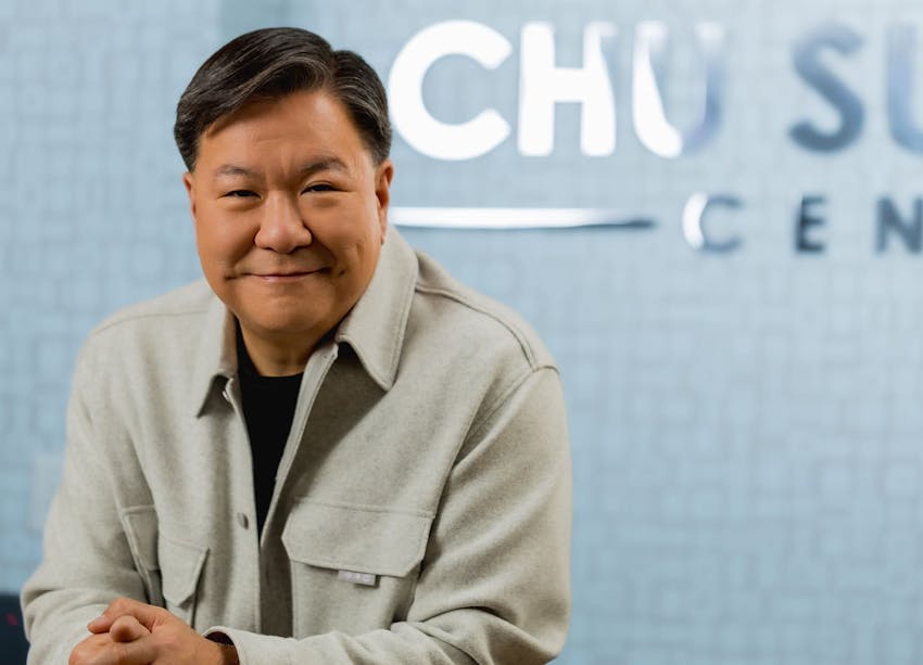 Dr. Chu smiling while sitting in front of his logo