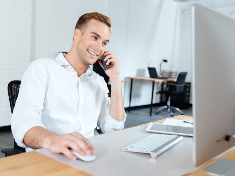 man sitting at a desk talking on a cell phone