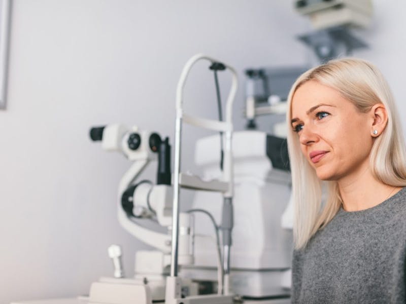blond woman in grey sweater looking at camera while sitting by eye exam equipment
