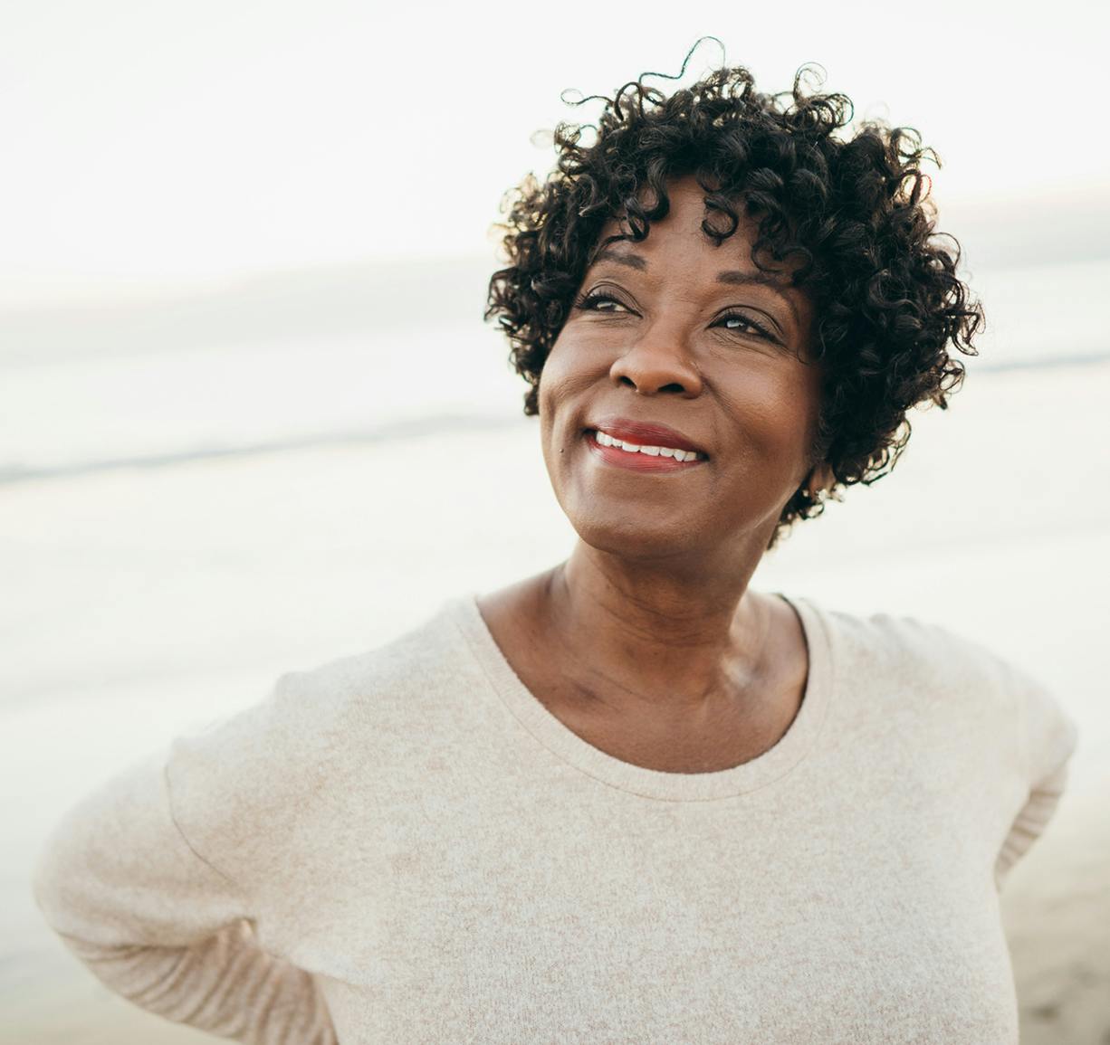 smiling woman with curly hair standing on beach with ocean in background