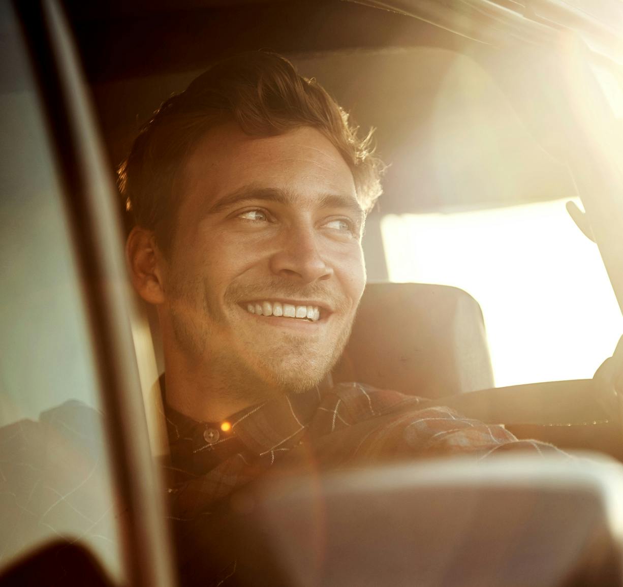 smiling man in a car with sun shining through the window