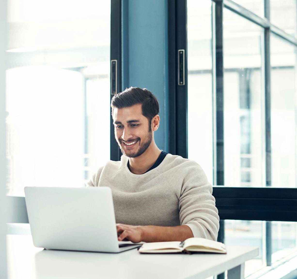 smiling man sitting at a table with a laptop computer in front of him
