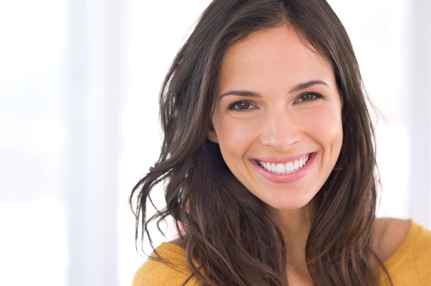 close up of a smiling woman with long brown hair and yellow sweater