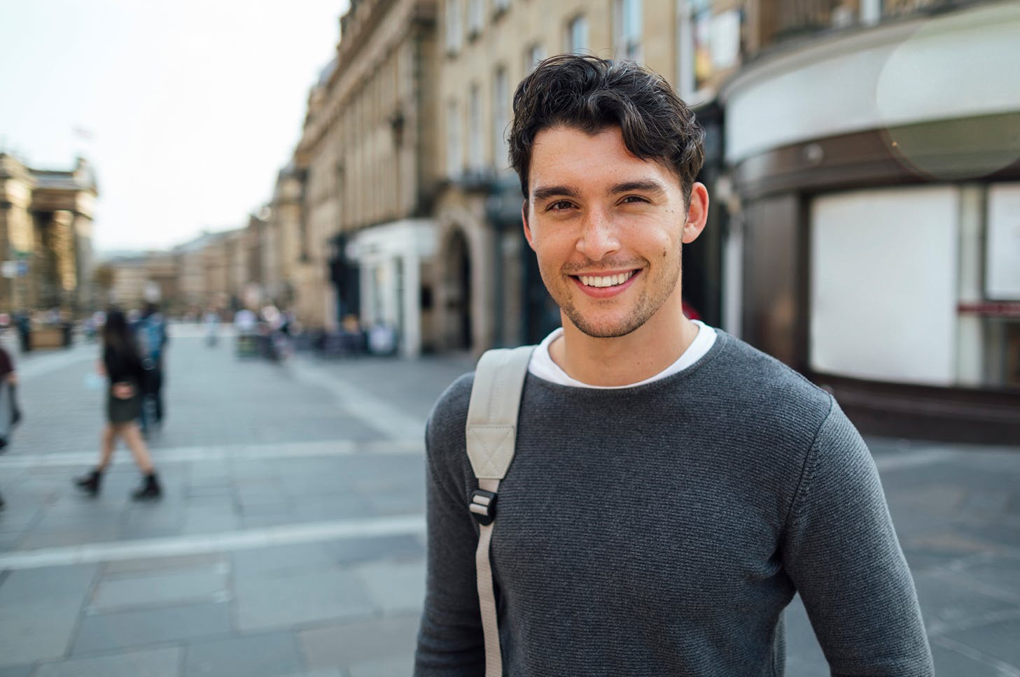 man in a gray sweater and a backpack standing in a city street