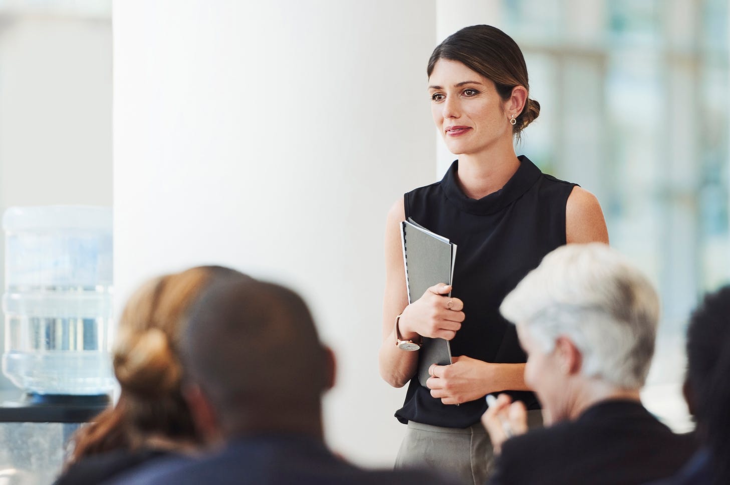 woman in black top holding a folder in front of a group of people