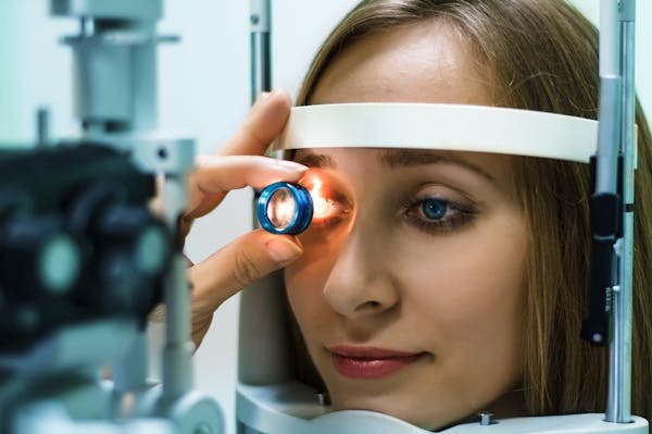 a woman receiving an eye exam with light shined in right eye