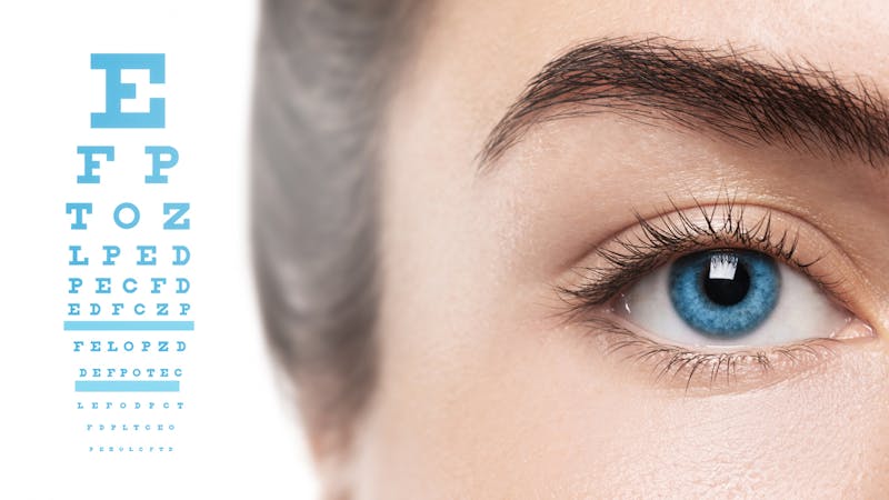 Close up of woman's right blue eye with a image of a Snellen chart in the background