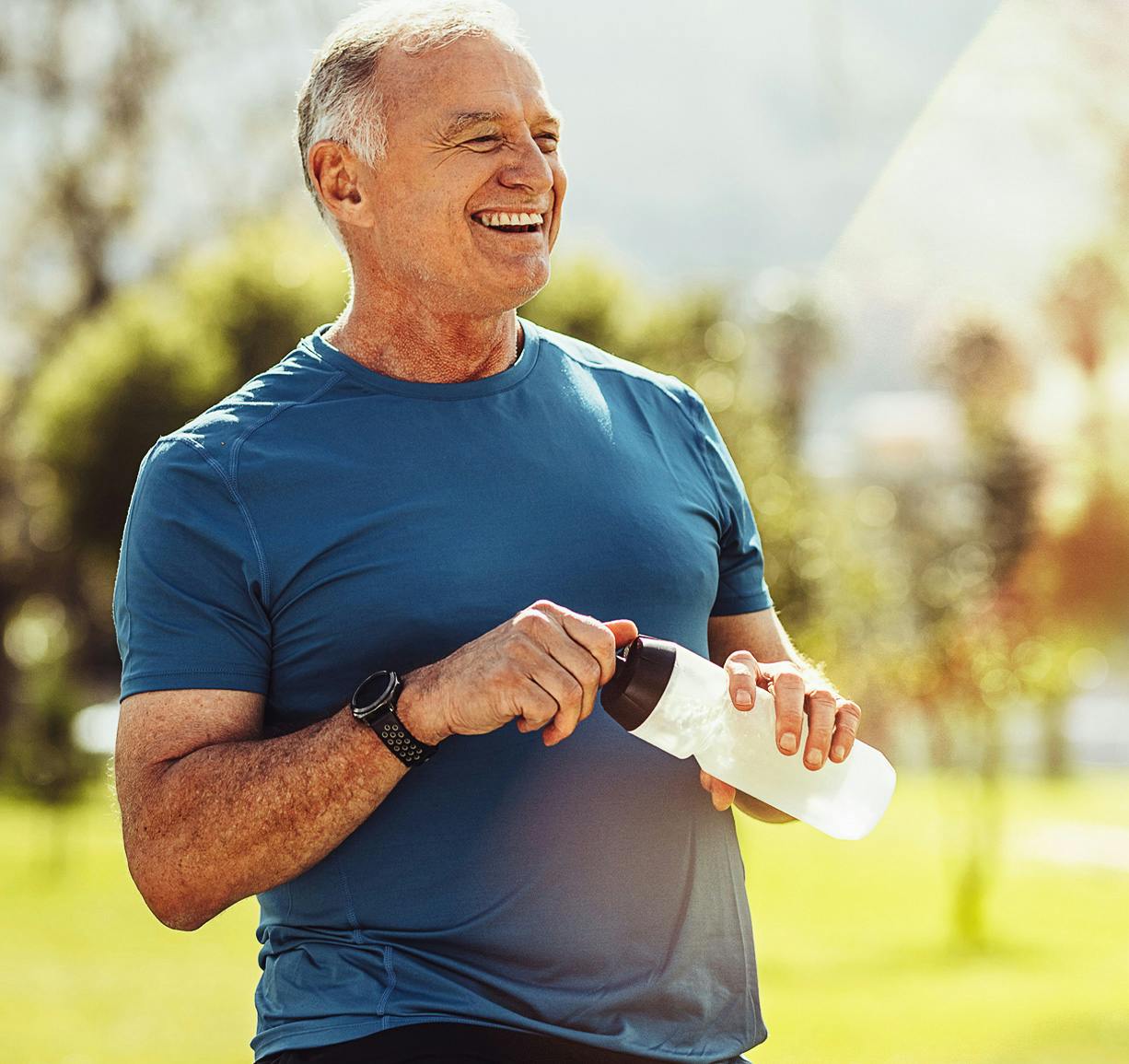 man in blue t-shirt holding a water bottle looking out and smiling