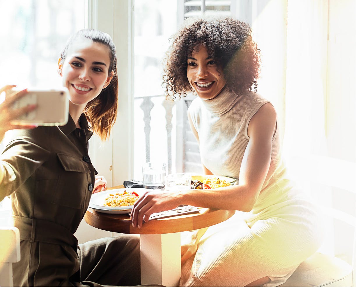 Two ladies having lunch smiling and taking a photo of themselves.