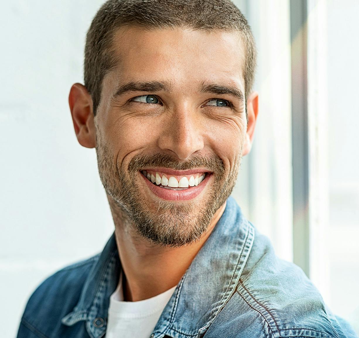 man smiling in denim jacket looking off to the side
