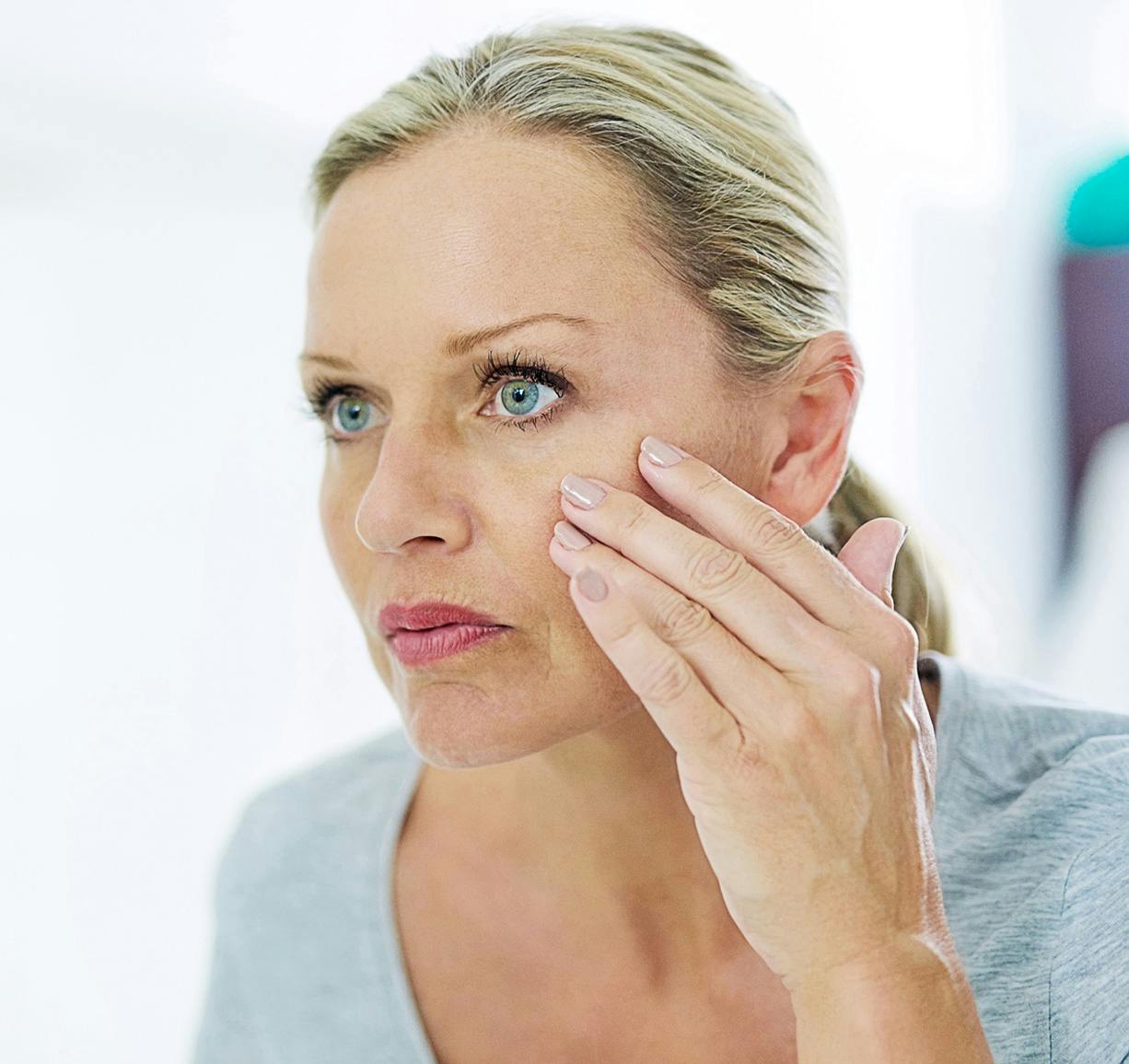 woman examining her eyes in the mirror