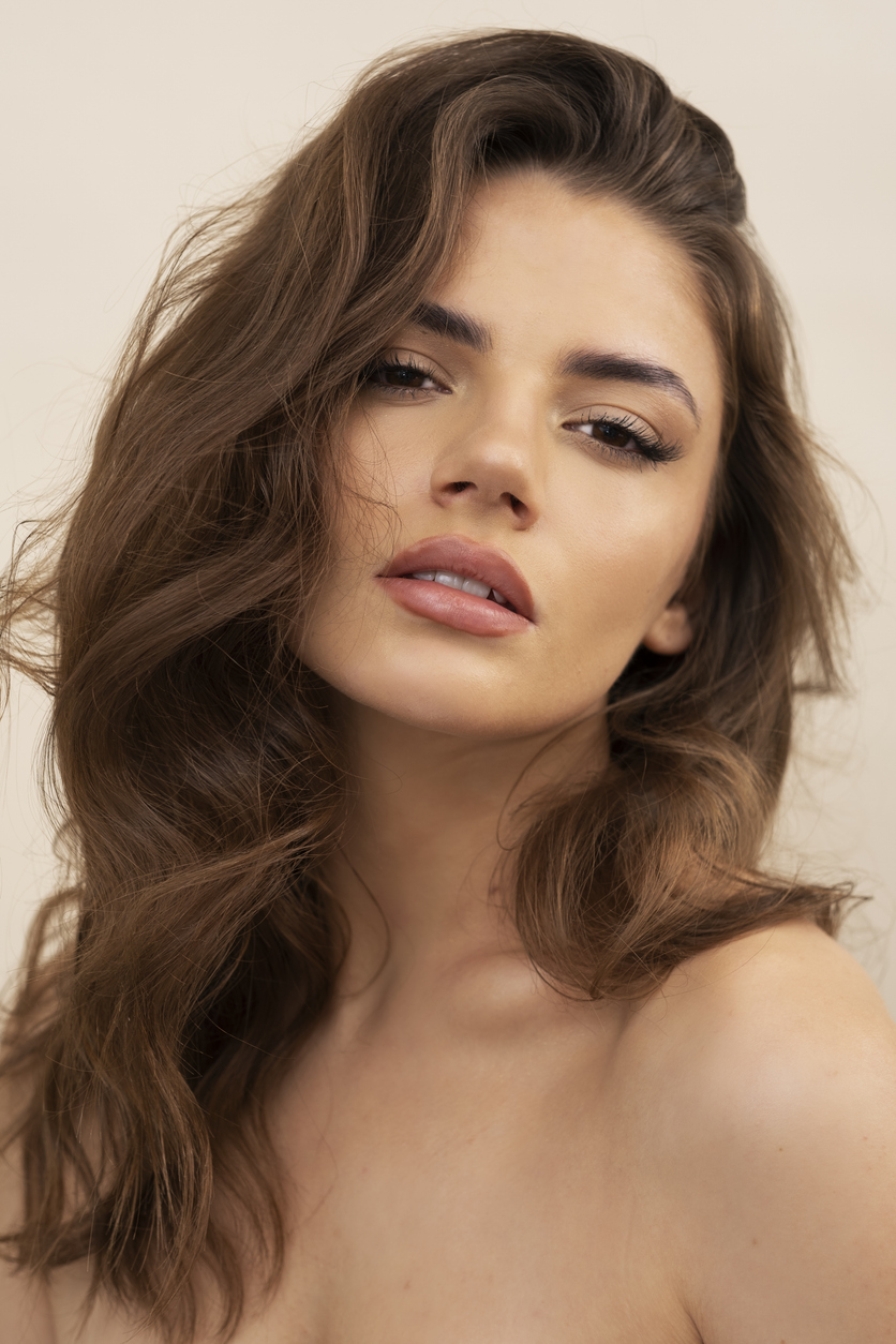 young woman with long hair looks seductively at camera. She has beautiful facial symmetry to show the potential results of a chin augmentation in Los Angeles