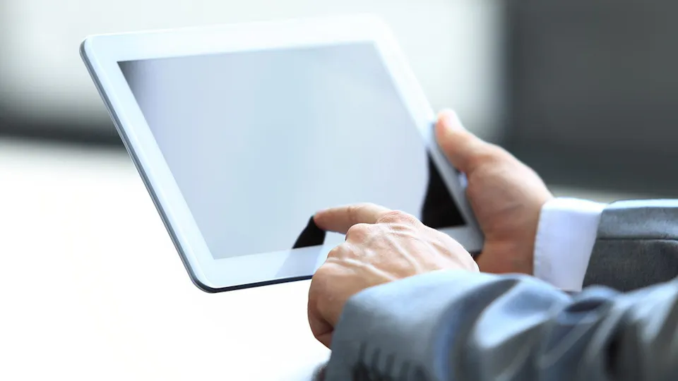 TFT industry A person in a suit holds a digital tablet with a blank screen, interacting with it using their index finger, set against a plain background.