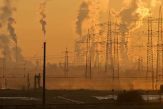 Fine dust in the industry The image depicts a sunset industrial landscape with numerous power lines and tall smokestacks releasing smoke, illustrating environmental pollution and industrial energy production.