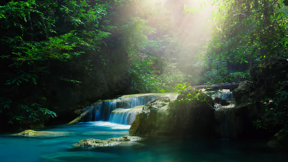 關鍵視覺 DAS 環境專家 水處理 - 清潔水 陽光斜射在翠綠叢林中的小瀑布和藍綠色溪流上,營造出寧靜的自然景觀。