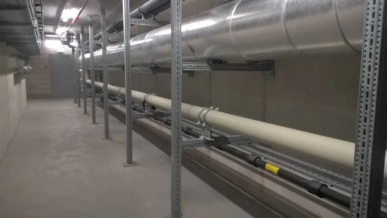 Biotest Reference Ein grauer, industriell wirkender Technikraum mit großen, silbernen Lüftungsrohren, die entlang der Betondecke und der Wände verlaufen.