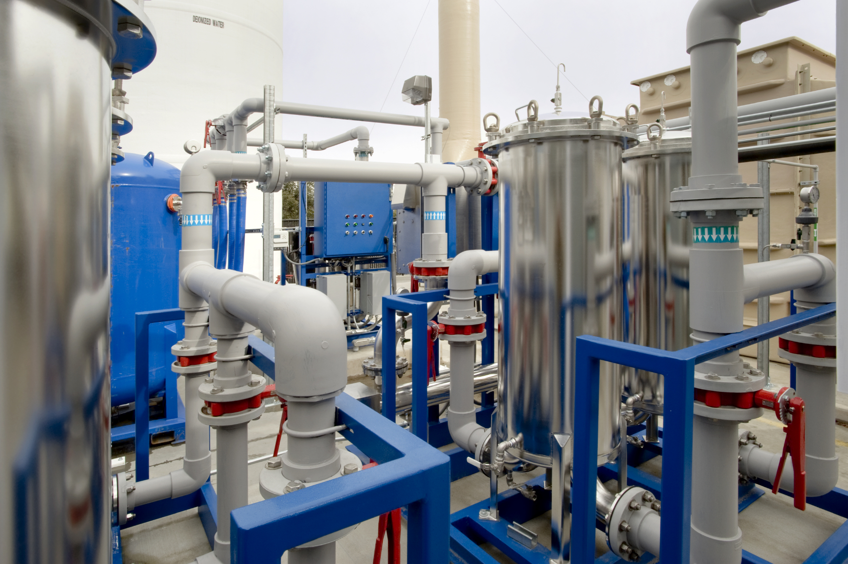 Industrial piping systems with shiny metal pipes and blue fittings assembled in a factory environment.