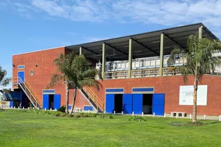 Reference Beverage industry A large brick building with blue garage doors stands on a lush green lawn, surrounded by palm trees and under a clear blue sky.