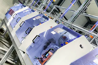 Teaser Cosmetics Manufacturer Several state-of-the-art dosing stations lined up in an industrial setting, standing on a metal rack and illuminated from above.