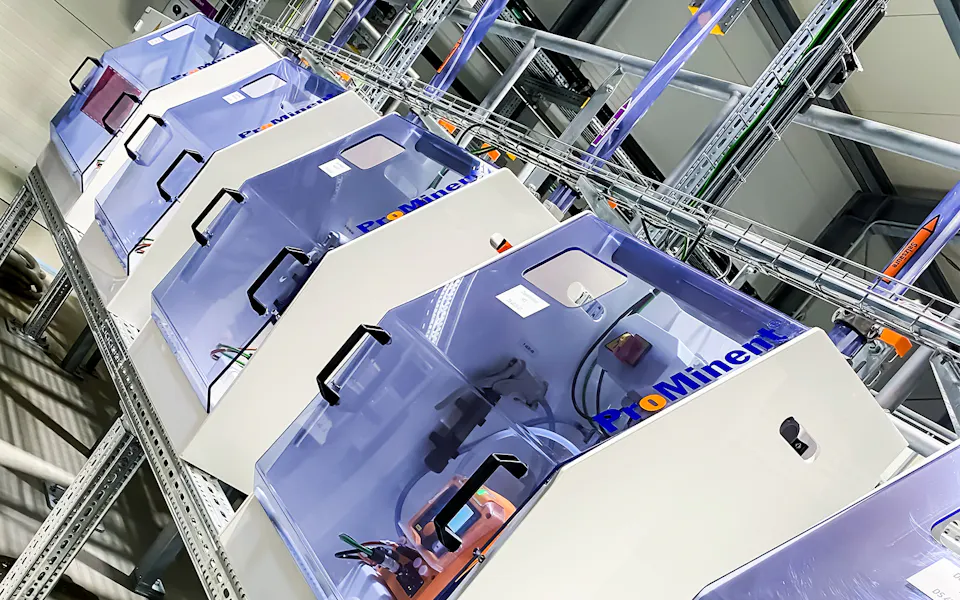 Teaser Cosmetics Manufacturer Mehrere hochmoderne Dosierstationen in einer industriellen Umgebung aufgereiht, während sie auf einem Metallregal stehen und von oben beleuchtet werden.