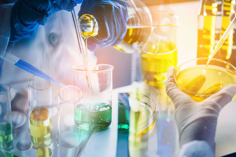 Laboratory technicians in a laboratory conduct chemical experiments with colored liquids in test tubes and Petri dishes while wearing protective clothing and gloves.