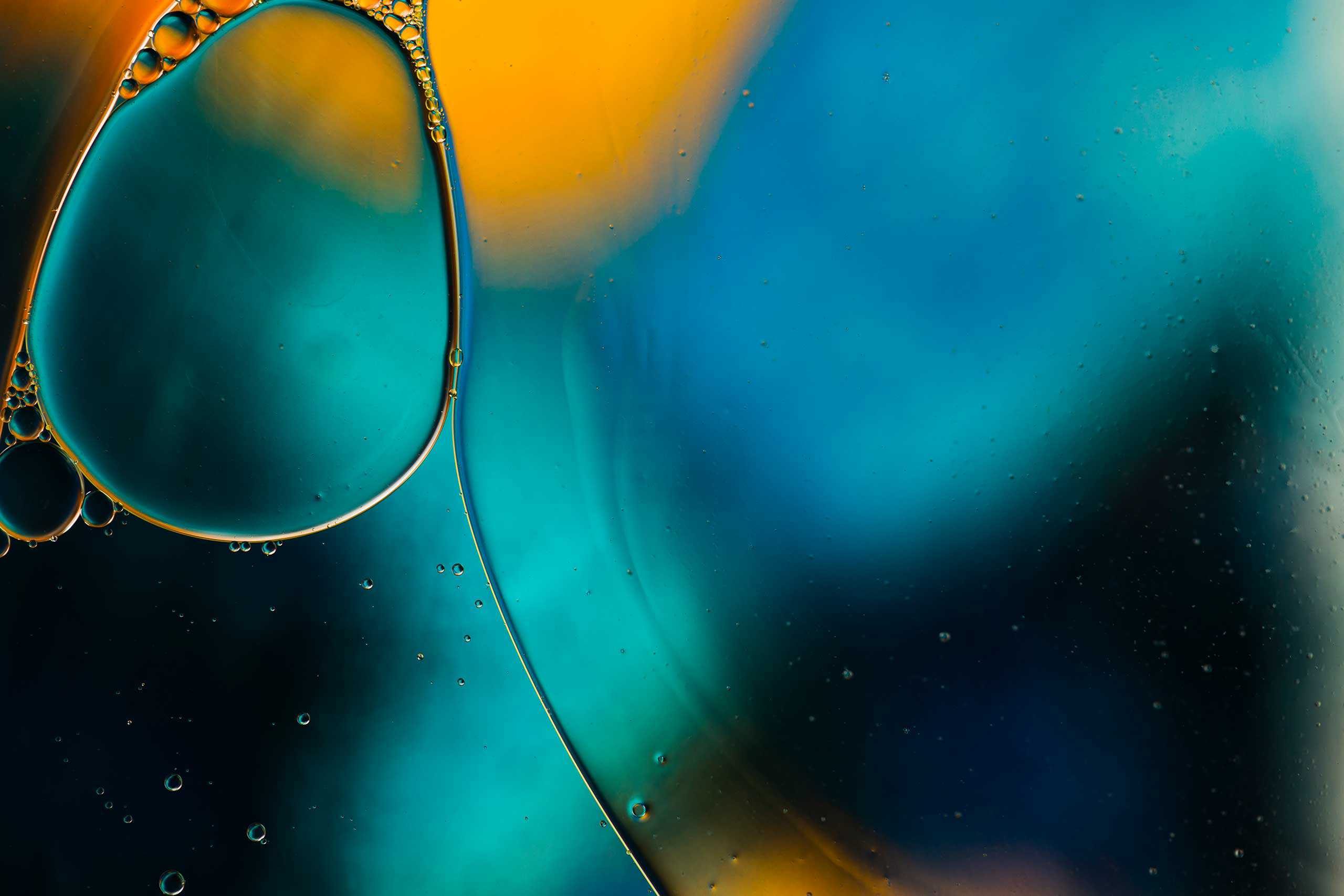 A close-up of colorful oil bubbles floating on water, featuring vibrant hues of orange and blue against a soft, blurred background.