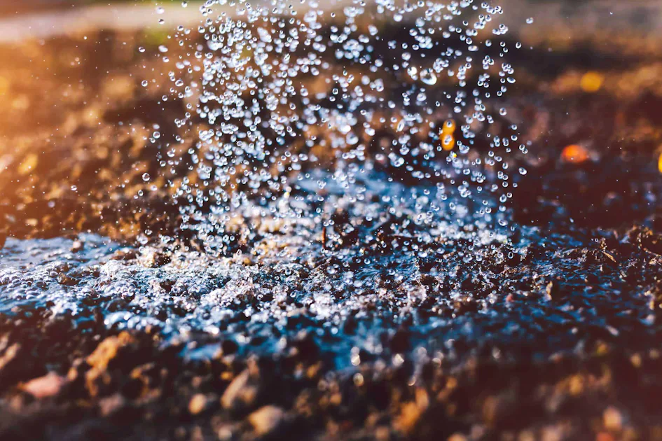Water droplets flowing on the ground Raindrops splatter on sunlit, muddy ground, creating a dynamic display of water droplets and splashes that reflect the light, highlighting the beauty of a refreshing rainfall in nature.