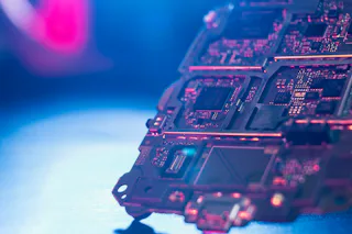 Semiconductor Industry A close-up of a computer circuit board illuminated by bright blue and pink lights reveals complex circuits and electronic components in a technological and futuristic setting.