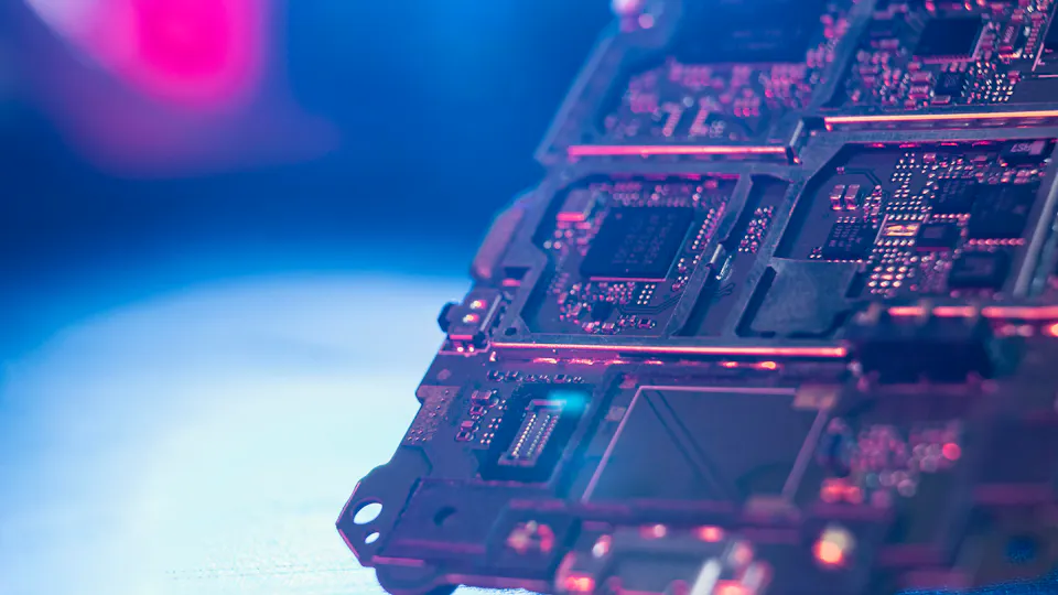 Semiconductor Industry A close-up of a computer circuit board illuminated by bright blue and pink lights reveals complex circuits and electronic components in a technological and futuristic setting.